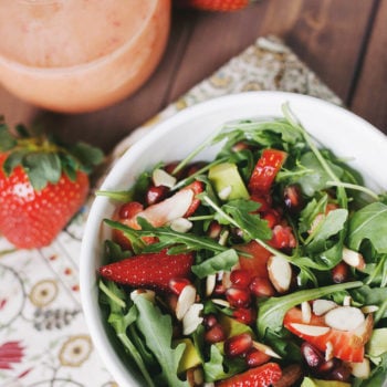 Strawberry salad on a napkin laying on a wooden board with strawberry dressing next to it.