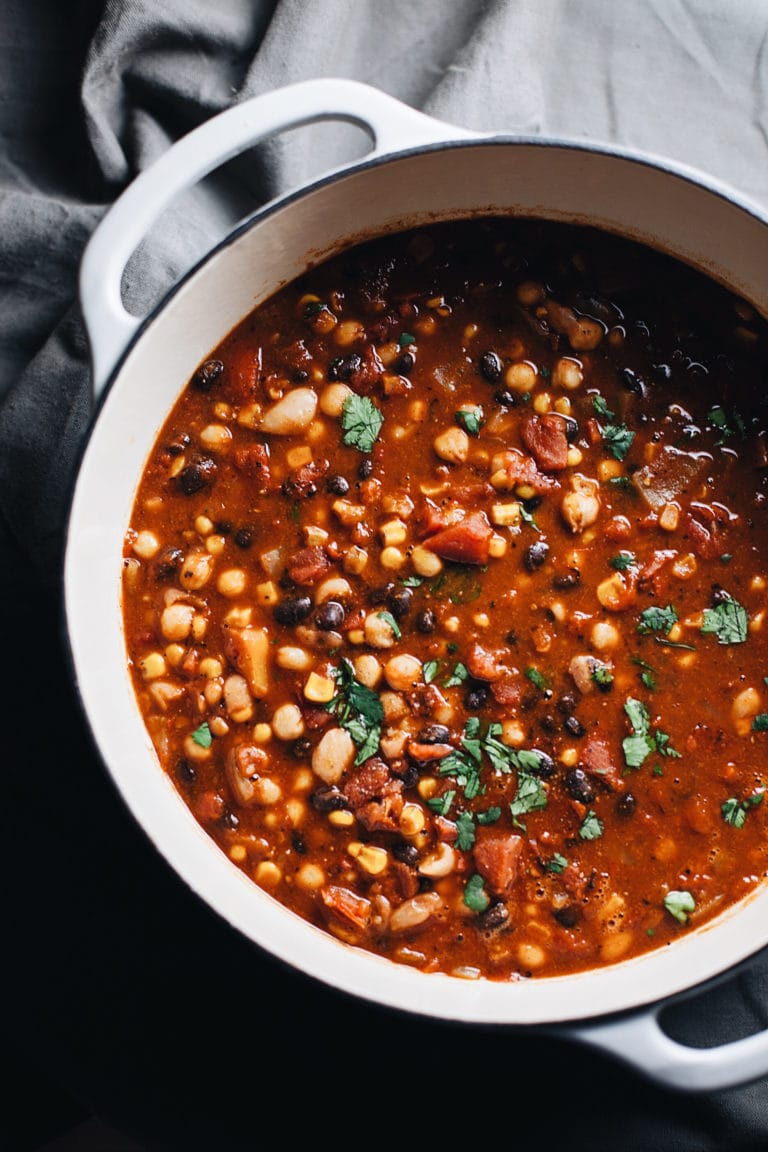 A white dutch oven with vegetarian bean chili in it.