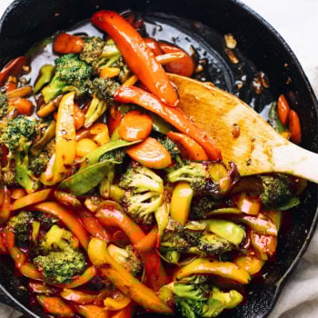 A black cast iron skillet with assorted vegetable stir fry and a wooden spoon in it.