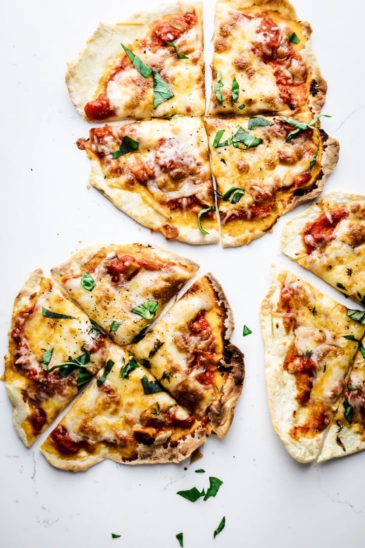 tortilla pizza on a white background sliced into 4 slices each with fresh basil sprinkled over top.