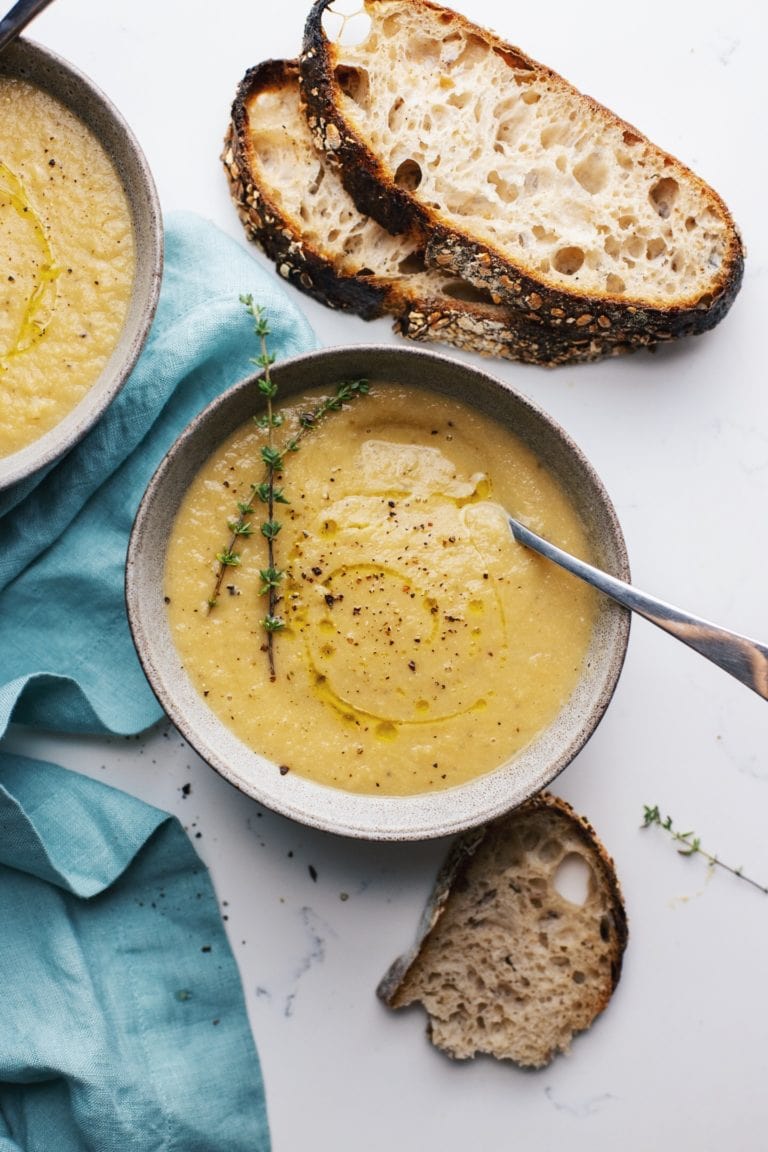 A grey bowl with cauliflower soup with a blue napkin and slices and bread next to it.