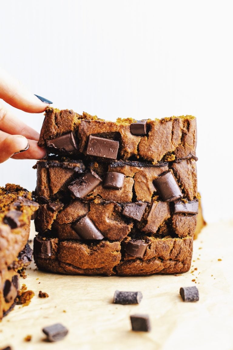 A hand picking up a top piece from a stack of healthy pumpkin bread slices studded with chocolate chunks.