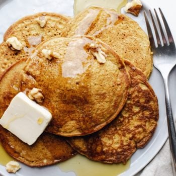 A close up of a stack of pumpkin spice pancakes with butter, drizzled maple syrup, and a fork next to it.