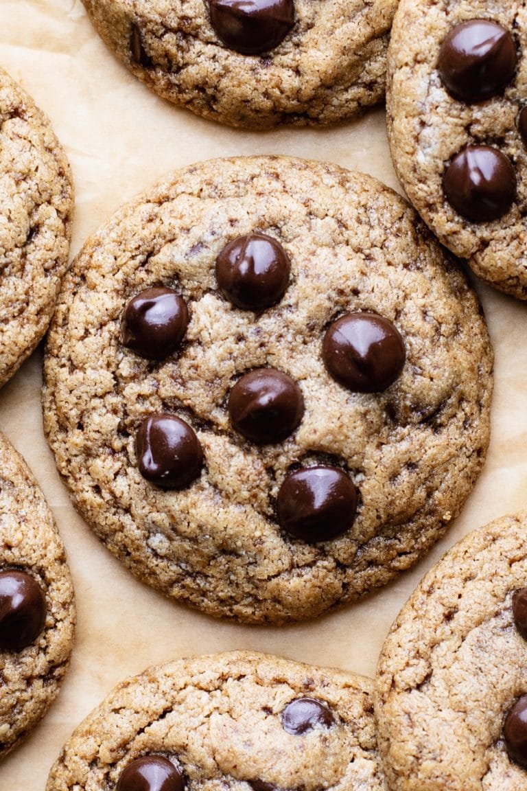 A close up of a gluten free peanut butter cookie with chocolate chips on brown parchment paper.