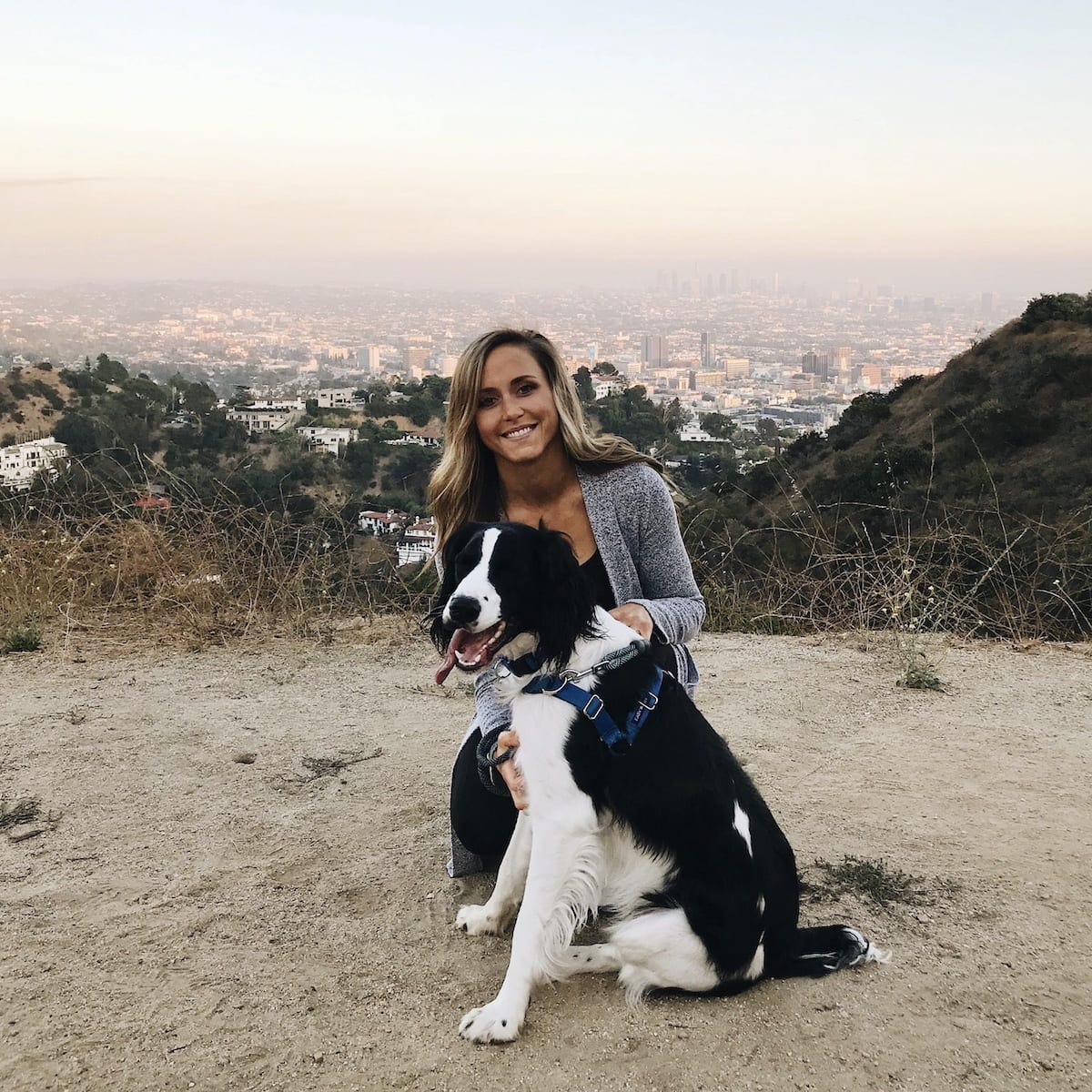 Hudson, a black and white English Springer Spaniel dog, and Bethany Kramer hiking at Runyon Canyon park overlooking downtown Los Angeles.