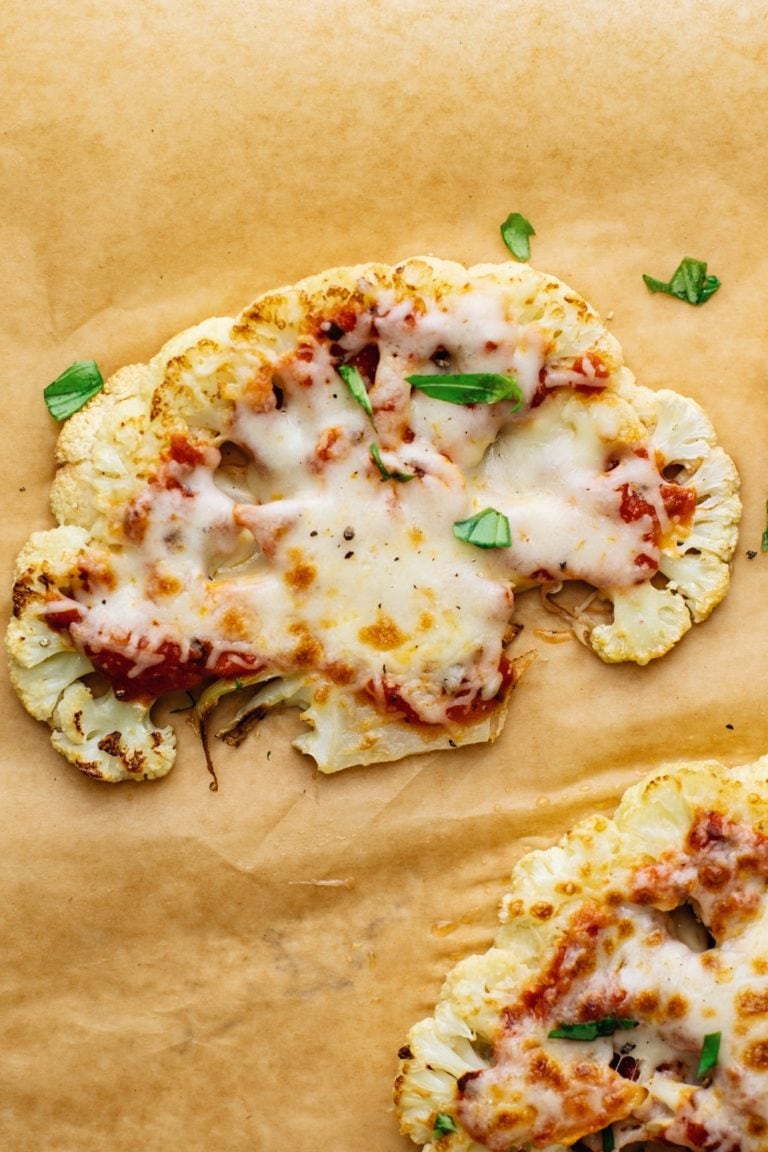 Cauliflower steak pizza arranged on brown parchment paper.