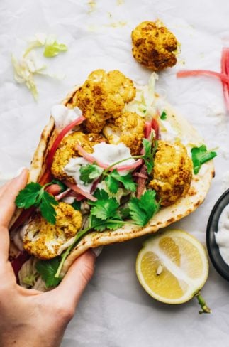 A hand holding a naan wrap with roasted cauliflower on white parchment paper.