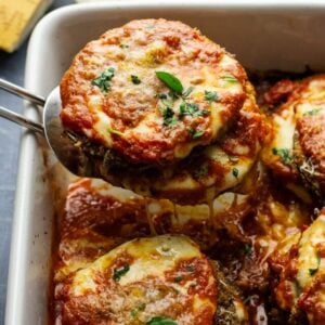 a slice of eggplant parmesan being lifted on spatula out of white baking dish.