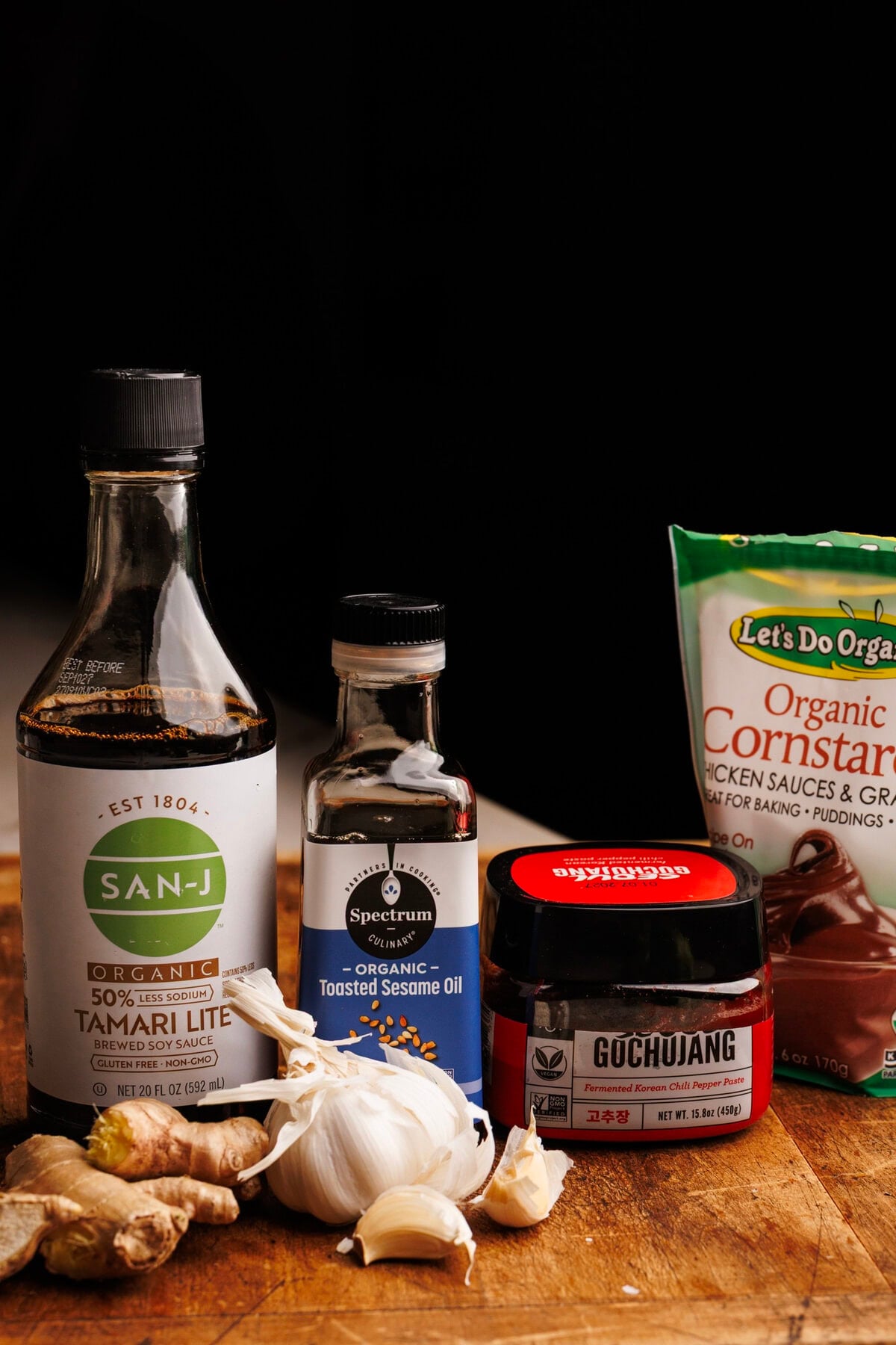 A photo of different asian condiments for beef and broccoli sauce arranged on a wooden board with a dark black background behind it.