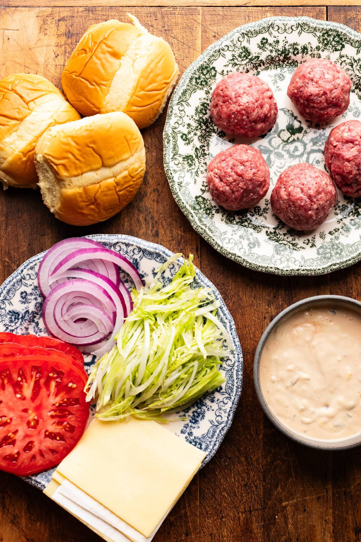 Ingredients for smash burgers arranged on plates and decorated on a wooden board.