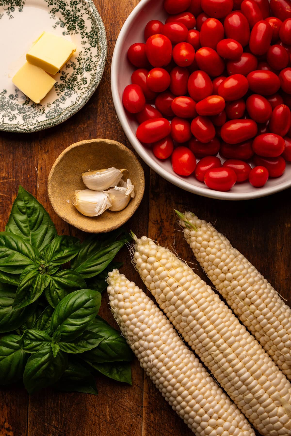 Ingredients for cooked corn and tomatoes arranged on a wooden background.