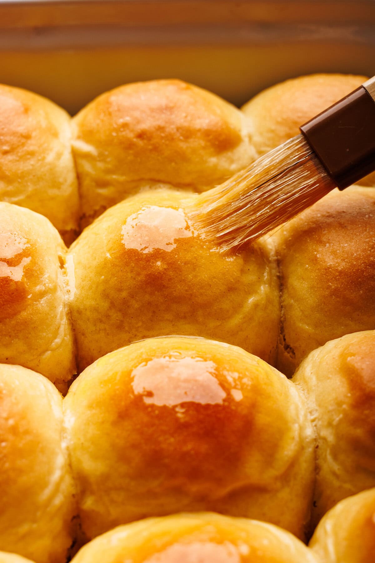 A close up of dinner rolls being brushed with melted butter.