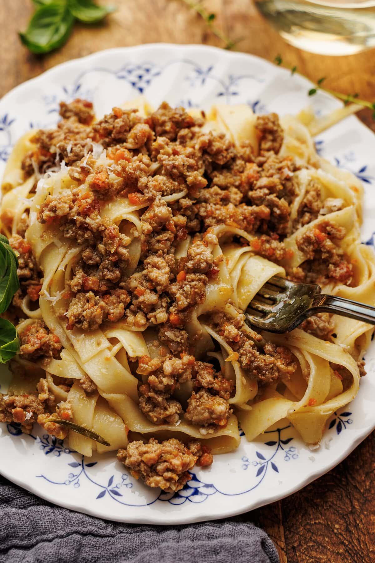 A close up of a fork twirling tagliatelle past with white bolognese sauce on a white plate.