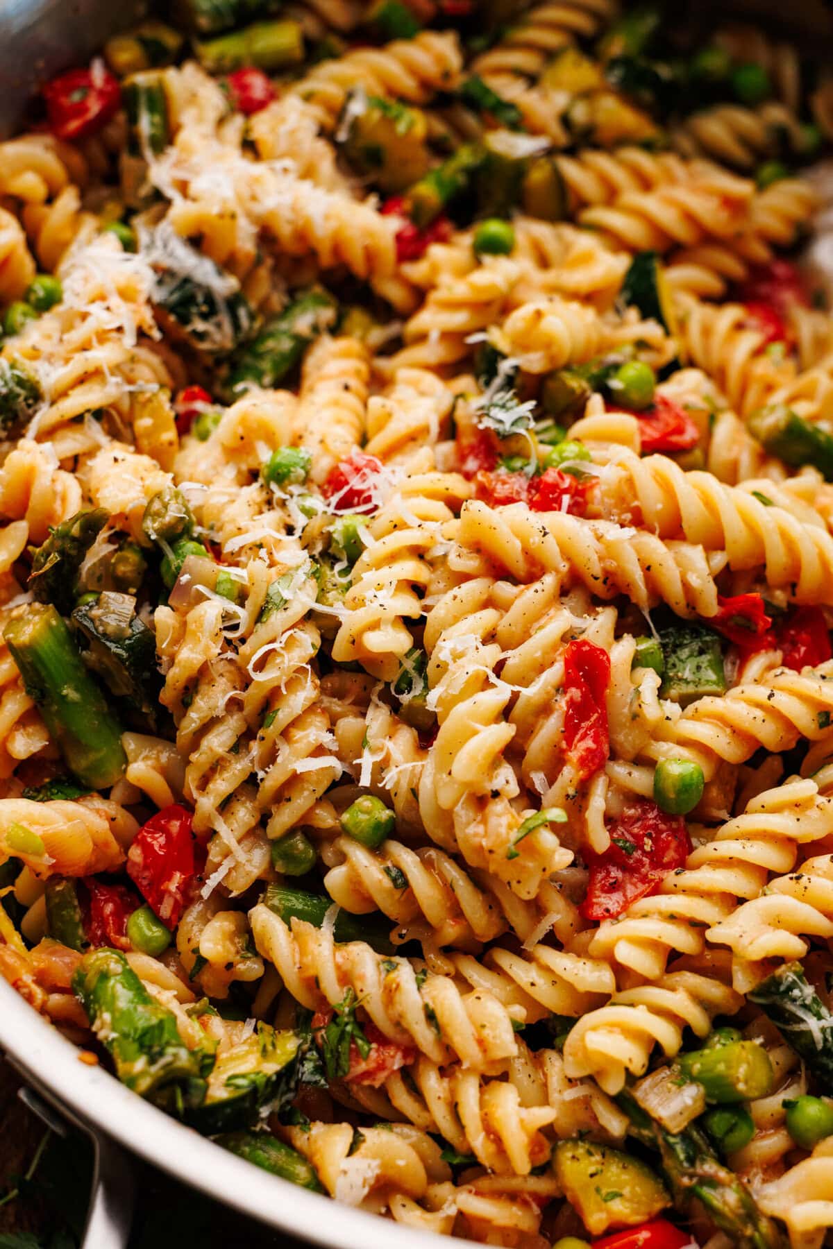 A close up of pasta primavera being stirred in a sauce pan with lots of vegetables.