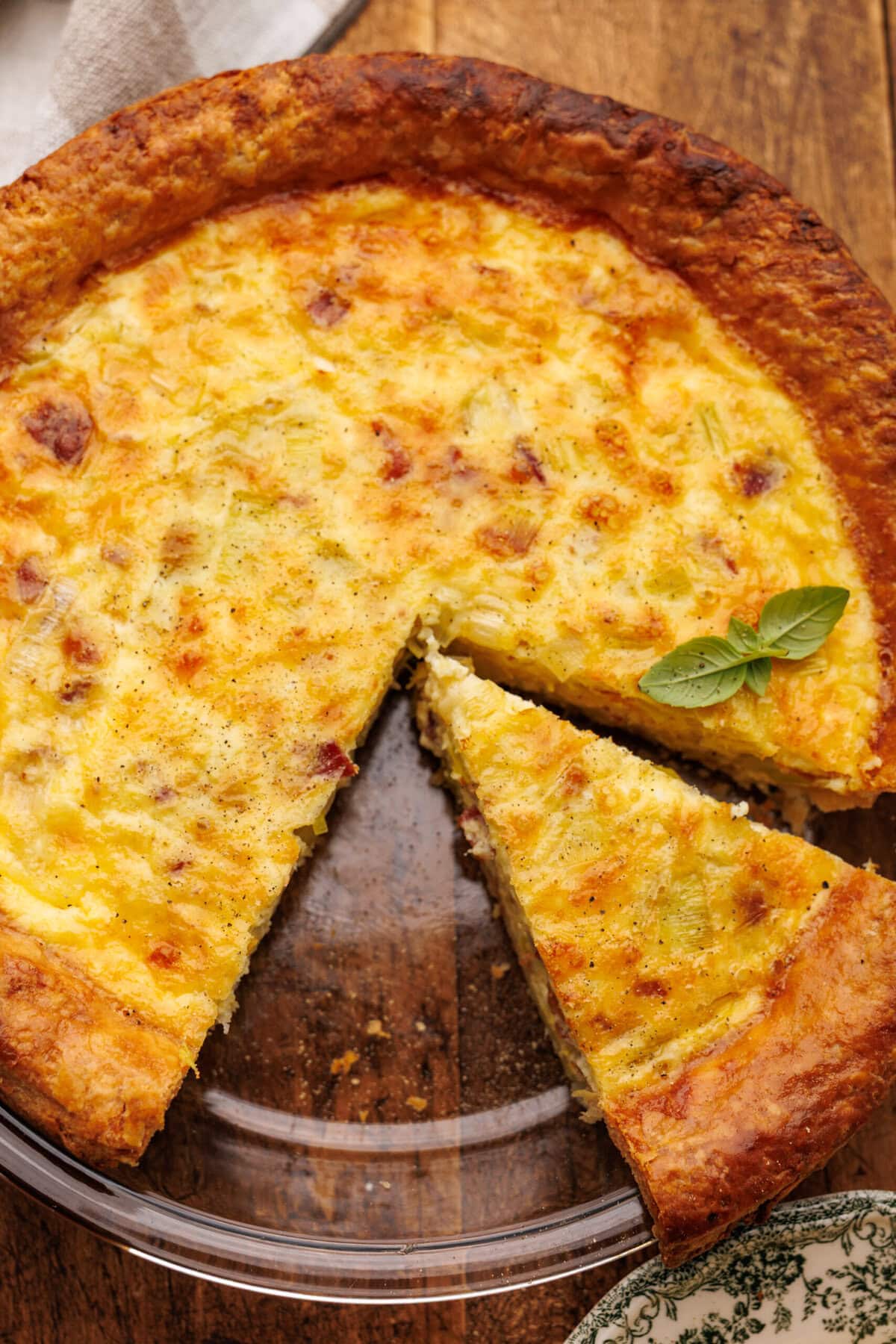 Quiche lorraine freshly baked with a slice cut out of it in a glass pie dish on a wood background.