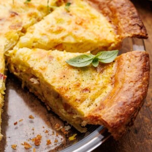Quiche lorraine freshly baked with a slice cut out of it in a glass pie dish on a wood background.