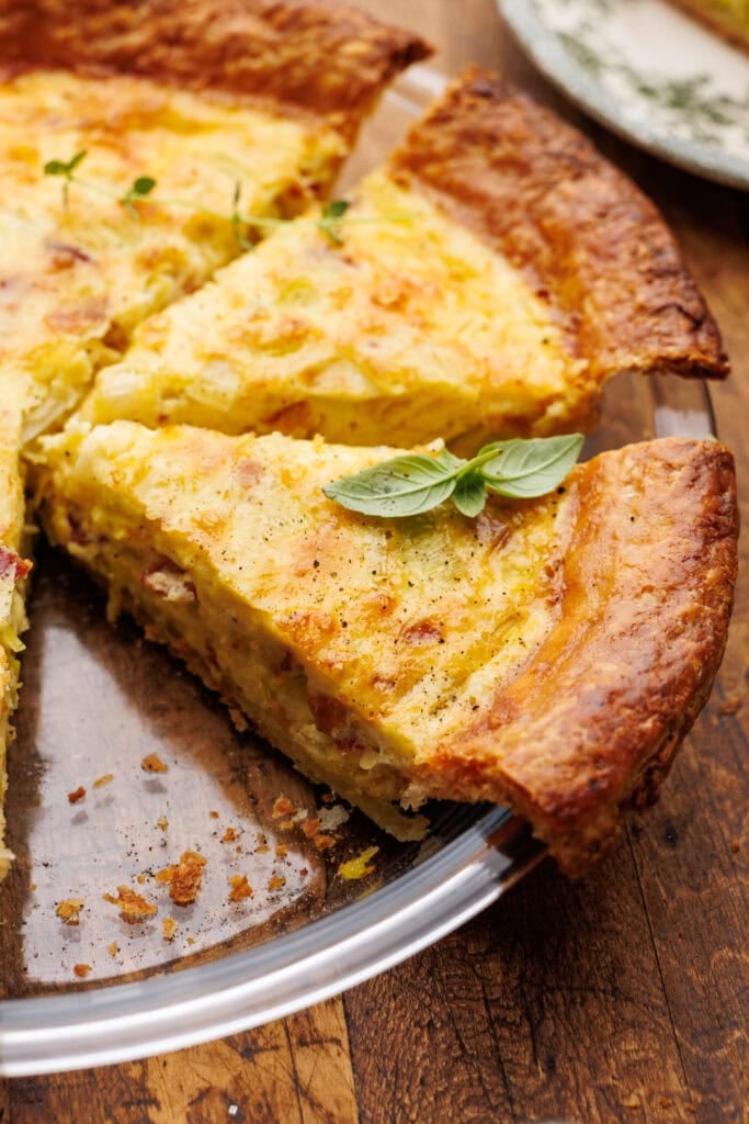 Quiche lorraine freshly baked with a slice cut out of it in a glass pie dish on a wood background.