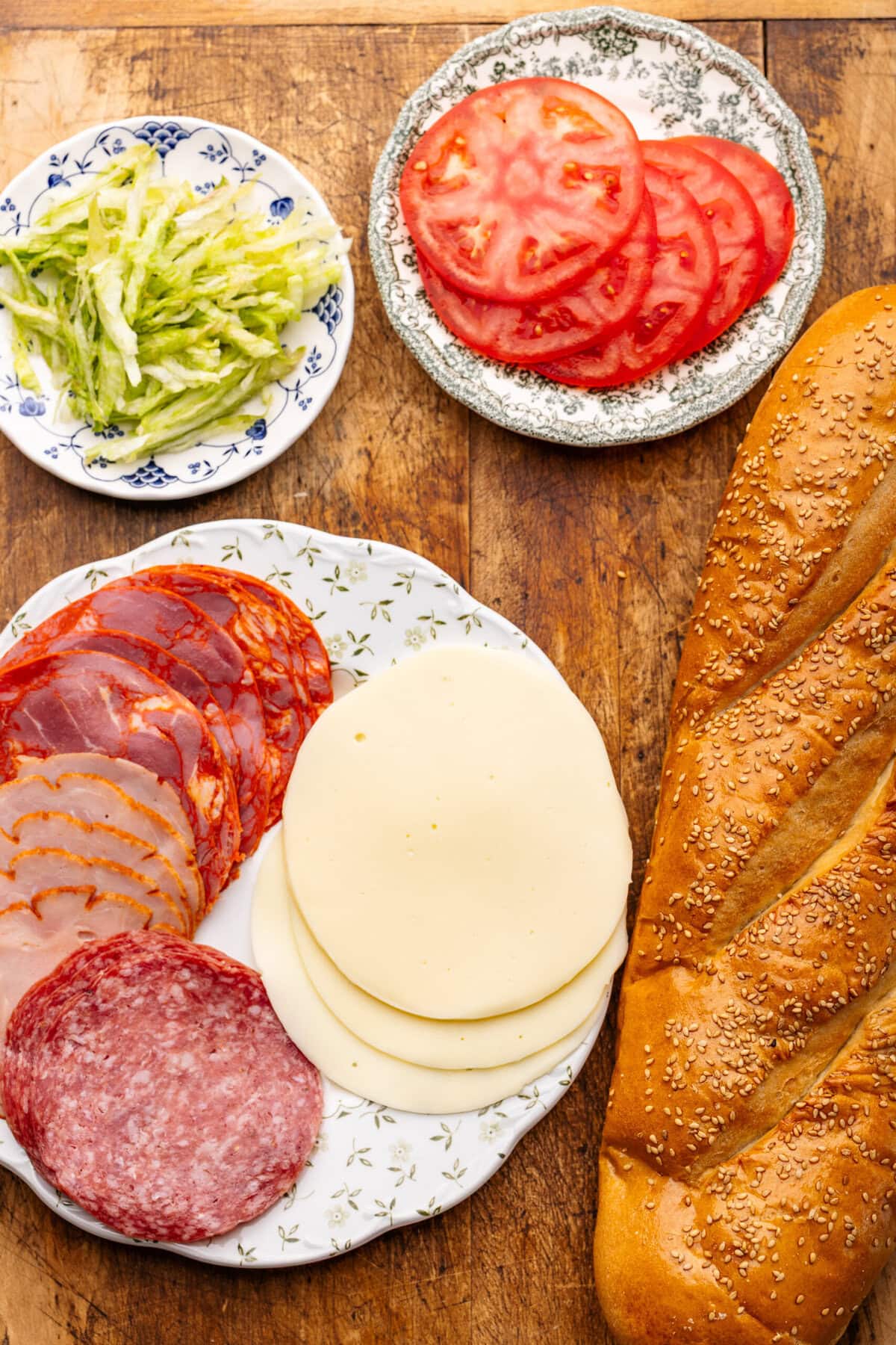 Italian sub ingredients arranged on plates and displayed on a wooden board.