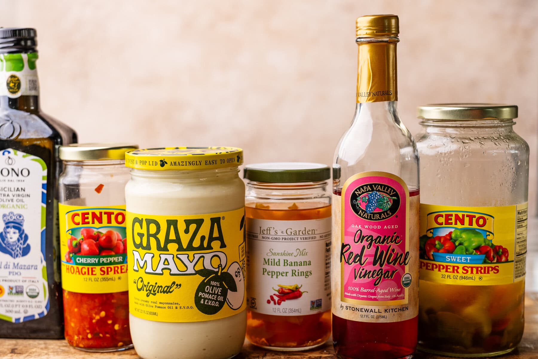 Topping ingredients for an Italian sub displayed in jars ranging from mayonnaise, pickled peppers, and olive oil and vinegar. 
