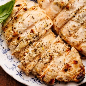 A close up of grilled lemon chicken sliced and displayed on a white and blue vintage plate thats on a wooden board.
