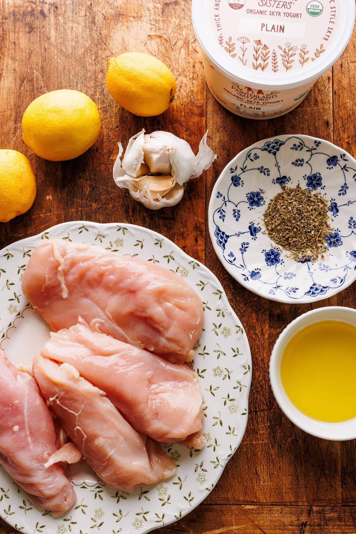 Ingredients for grilled lemon chicken arranged on a wooden brown board.