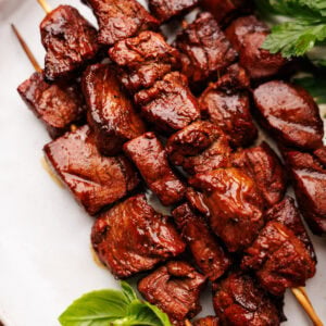 Steak kabob's on a white plate with fresh green herbs placed around them.