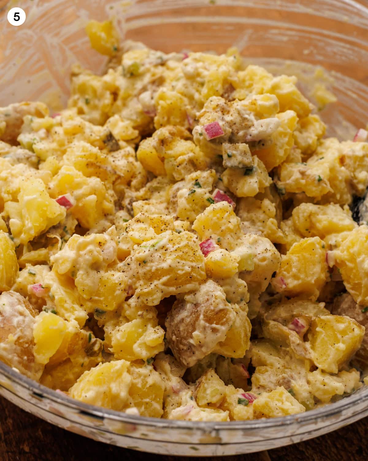 A single photo, labeled step five, showing the finished potato salad in a glass bowl. The chunks of potato are fully coated in creamy dressing with red onion, chives, and celery throughout, and the top is dusted with coarsely ground black pepper. See task progress for longer tasks. alt-text.md potato-salad-alt-text.md Potato Salad