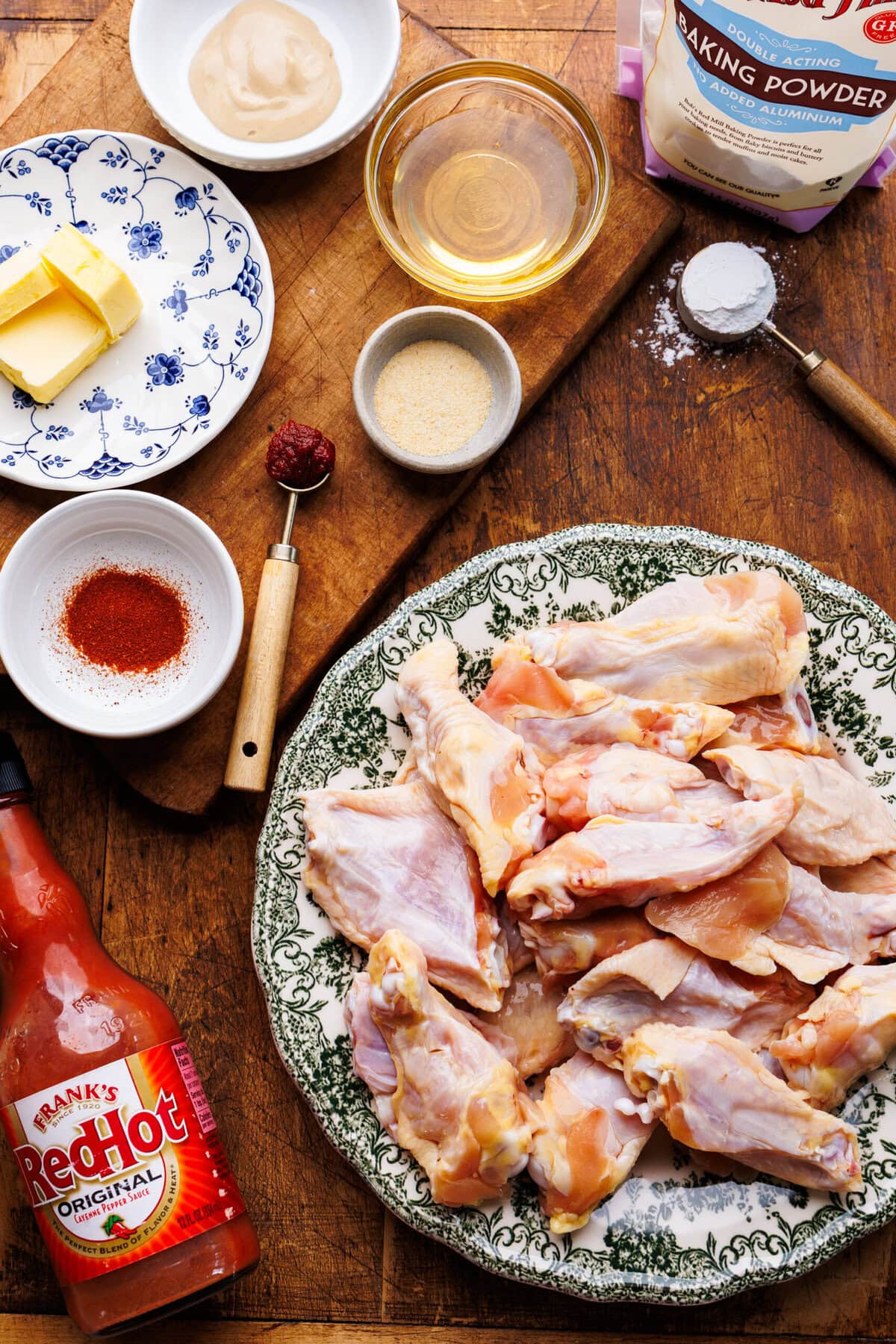 Ingredients for buffalo wings recipe on a wooden board, including chicken wings, Franks hot sauce and more.