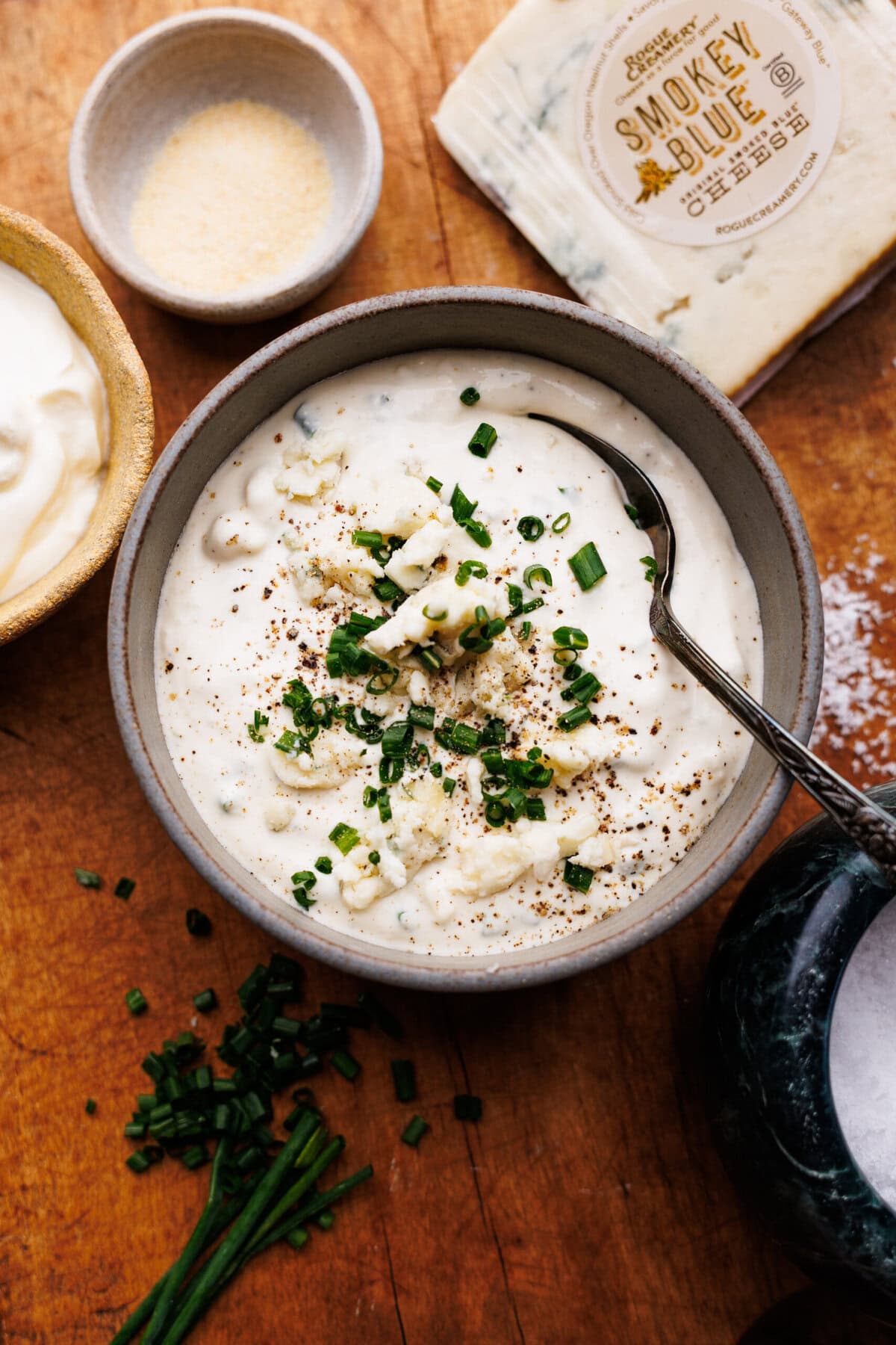 Blue cheese dip for wings in a bowl on a wooden cutting board surrounded by the ingredients